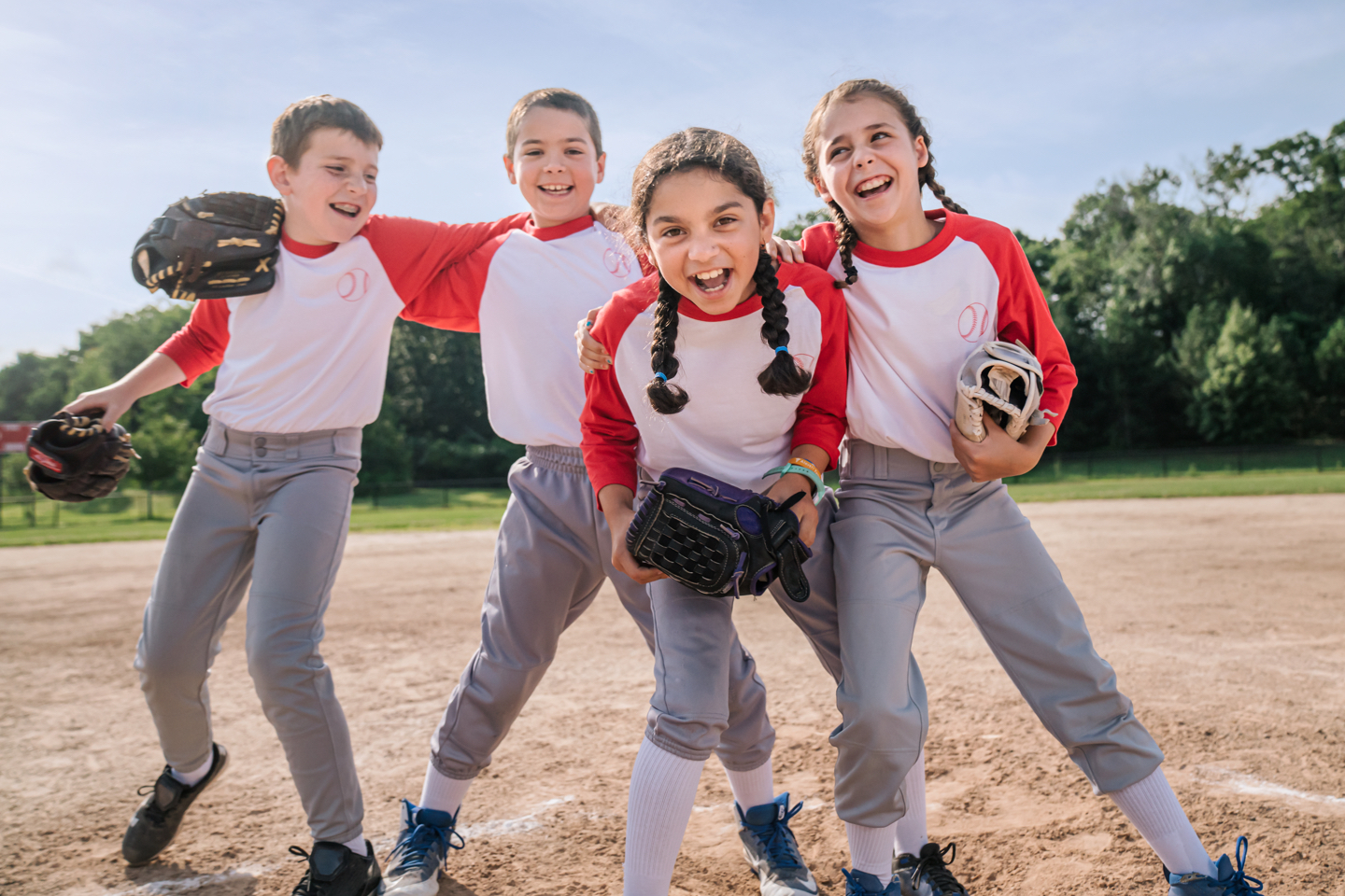 Four children in baseball uniforms on a field.